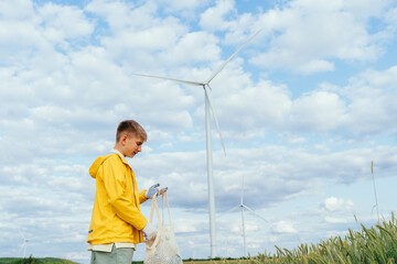 Teenager holding mesh bag with plastic waste near wind turbines