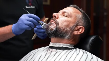 Skilled barber applies shaving cream to a client's beard, ensuring a precise shave in a warm, inviting barbershop atmosphere, showcasing expert grooming techniques