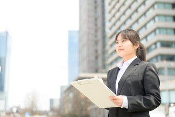 屋外でバインダーを持つリクルートスーツの日本人女性