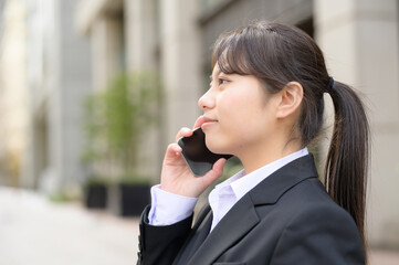 ビル街で電話をするリクルートスーツの日本人女性