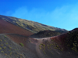Majestic view of Mount Etna's volcanic landscape in Sicily, bathed in the warm hues of the setting sun. The rugged terrain showcases a blend of deep reds, oranges, and purples.