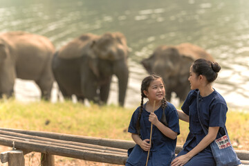 Asian mother and daughter in indigo clothing spending time in elephant conservation, family...