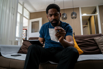 Worried young black man at home feeling stressed about cost of living, rent and food prices,...