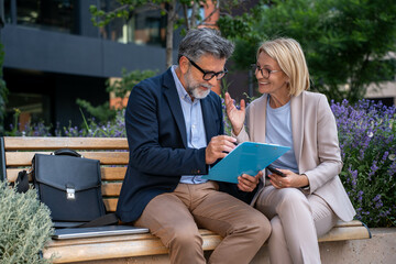 Businessman and businesswoman happily analyzing successful project outcomes outdoors in urban...