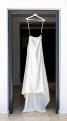 Elegant White Wedding Dress Hanging in Doorway Against Dark Background