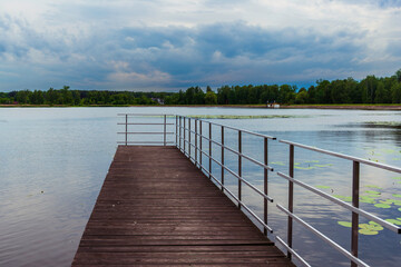 A scenic view of a wooden pier with metal railings extending into a tranquil lake surrounded by...