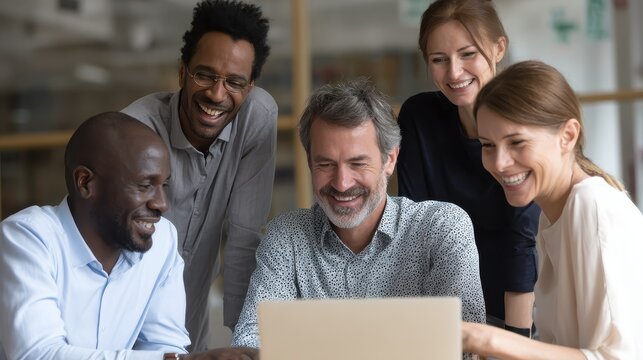 Smiling group of diverse businesspeople going over paperwork together and working on a laptop at a table in an office, no logos, no brands