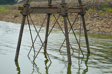 Weathered Rusty Metal Industrial Structure Submerged in Calm Water Near a Rocky River Bank