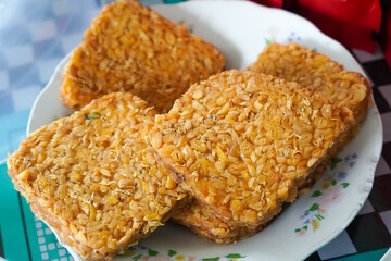 Golden Brown Fried Tempeh Slices on White Plate with Checkered Background