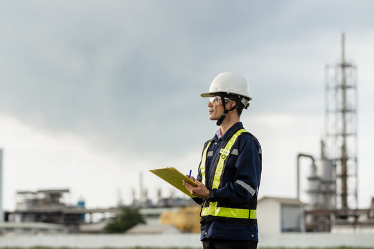 Safety Officer or Engineer Conducting an Inspection with a Clipboard. A man wearing a yellow vest and a hard hat is holding a clipboard