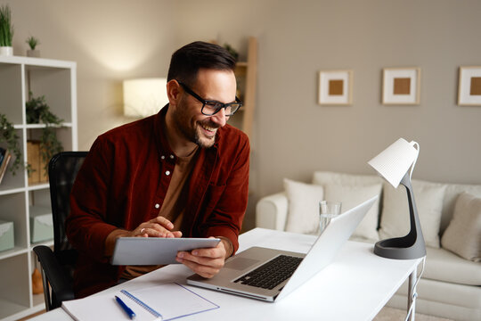 Freelancer smiling and working from home using laptop and tablet