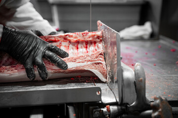 Close-Up of Butcher Slicing Raw Meat with Bandsaw in Meat Processing Plant