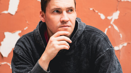 A young man with short brown hair is resting his chin on his hand lost in thought He is dressed in...