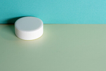 Single white medicine tablet laying isolated on green and blue pastel background as macro with copyspace 1