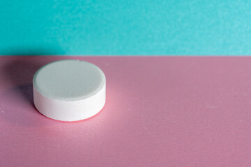 Single white medicine tablet laying isolated on pink and blue pastel background as macro 1