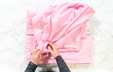 Hands Folding Pink Bed Sheet on Marble Surface