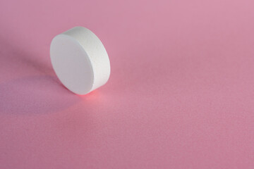 White medicine tablet standing on side on isolated on pink pastel background as macro 1