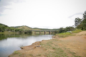 Foto de uma ponte cruzando uma represa em meio à natureza. As águas calmas refletem a estrutura e a vegetação ao redor, compondo uma cena tranquila e harmônica. Ideal para temas de infraestrutura, mei