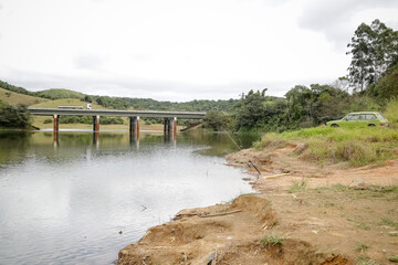 Foto de uma ponte cruzando uma represa em meio à natureza. As águas calmas refletem a estrutura e a vegetação ao redor, compondo uma cena tranquila e harmônica. Ideal para temas de infraestrutura, mei