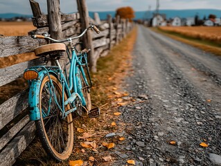 Vintage blue bicycle leaning against a rustic fence on a gravel road in autumn.