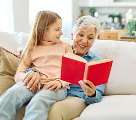 Portrait of grandmother and granddaughter having fun together reading a book at home