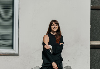 Smiling young caucasian female in black outfit standing outdoors by white wall