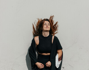 Confident young caucasian female with flowing red hair standing against white wall