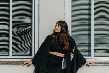 Female adult relaxing outdoors in stylish black outfit against a modern window