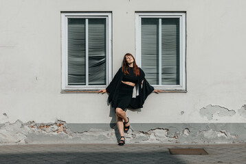 Female leaning against urban wall with windows in stylish outfit