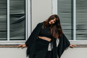 Young caucasian female in black outfit posing against windowed wall