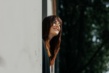 Fototapeta premium Young caucasian female smiling while leaning out a window in natural light