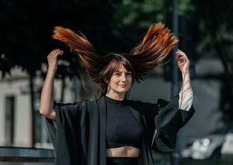 Young caucasian female flipping long red hair outdoors in stylish black outfit