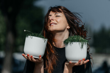 Young caucasian female joyfully holding plants outdoors with eyes closed
