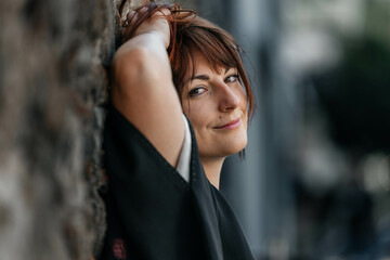 Smiling young caucasian female leaning against wall outdoors