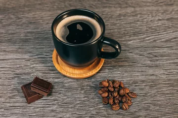 Tasse de café noir avec soucoupe en bois et grains de café et carrés de chocolat sur une table grise en bois - scène de petit déjeuner conviviale vue de haut