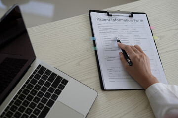 Young asian woman doctor in white uniform with stethoscope taking notes, using laptop, mobile phone, writing in medical journal, professional therapist practitioner filling documents or patient card.