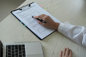 Young asian woman doctor in white uniform with stethoscope taking notes, using laptop, mobile phone, writing in medical journal, professional therapist practitioner filling documents or patient card.