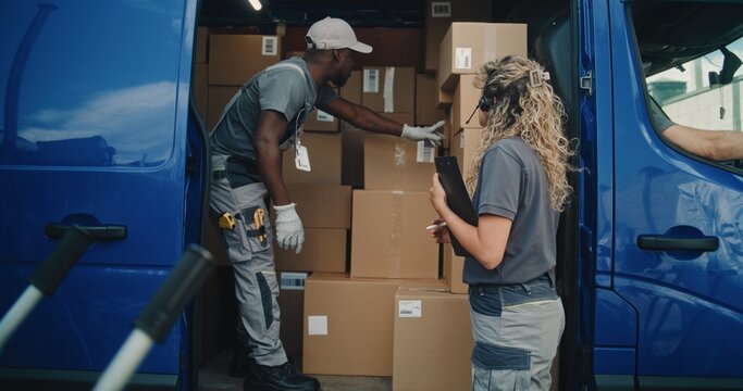 Outside of Logistics Distribution Warehouse: African American Employee Unloading Delivery Truck with Cardboard Boxes with Female Inventory Manager. Online Orders and E-Commerce Goods. Delivery Service