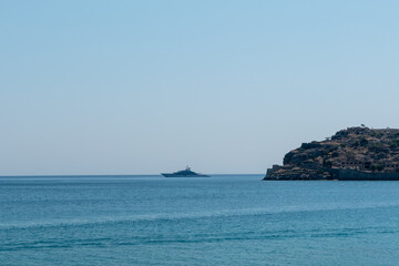 Large luxury yacht cruising on calm blue waters, with a rocky island to the right under a clear cloudless sky