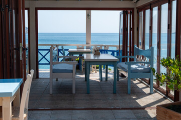 Inviting open-air restaurant with blue and white tables and chairs on beautiful panoramic view of calm blue sea. Greece, Crete, June, 21, 2025