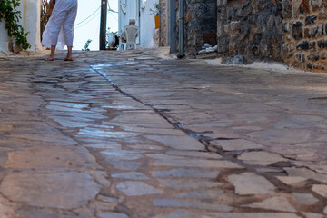 Narrow sunlit cobblestone alleyway in traditional village with an individual's bare feet visible in...