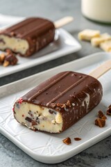 Chocolate-dipped ice cream popsicle with nuts and fruit bits, served on a white plate – a creamy frozen dessert perfect for summer indulgence.