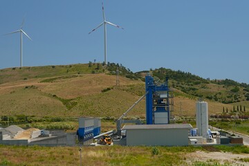 Wind turbines on the hills above a modern asphalt plant. Contrast between renewable energy and...