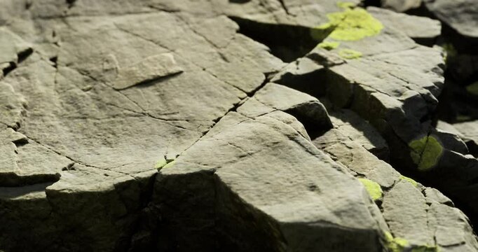 Close up of a rocky surface displaying detailed cracks and crevices, with patches of bright green moss adding a touch of color, highlighting nature textures and patterns.