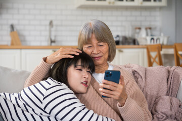 Senior mother and daughter sitting on the sofa at home, looking at a smartphone screen together....