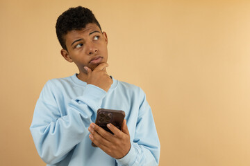 Dark skinned Latino teenager wearing a pastel blue sweatshirt with a thoughtful expression while...