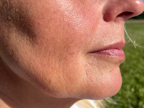 Detailed macro photo of mature woman’s cheek and chin showing natural skin texture, fine lines, mild pigmentation and pores in sunlight. Ideal for dermatology, skincare, or aging gracefully concepts.