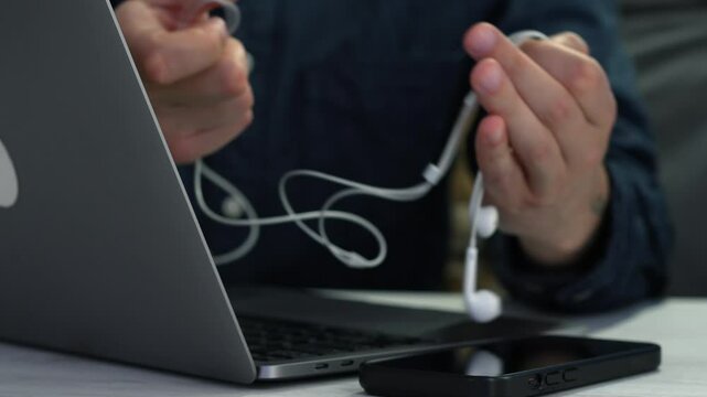 earphones in the hands of a guy sitting at a desk.
A man connects headphones to a laptop.
Headphone cable and listening to music