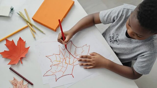 Young african male child drawing leaf with crayons on paper at home.