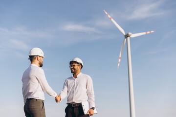 Engineers shaking hands in front of wind turbine, celebrating sustainable energy